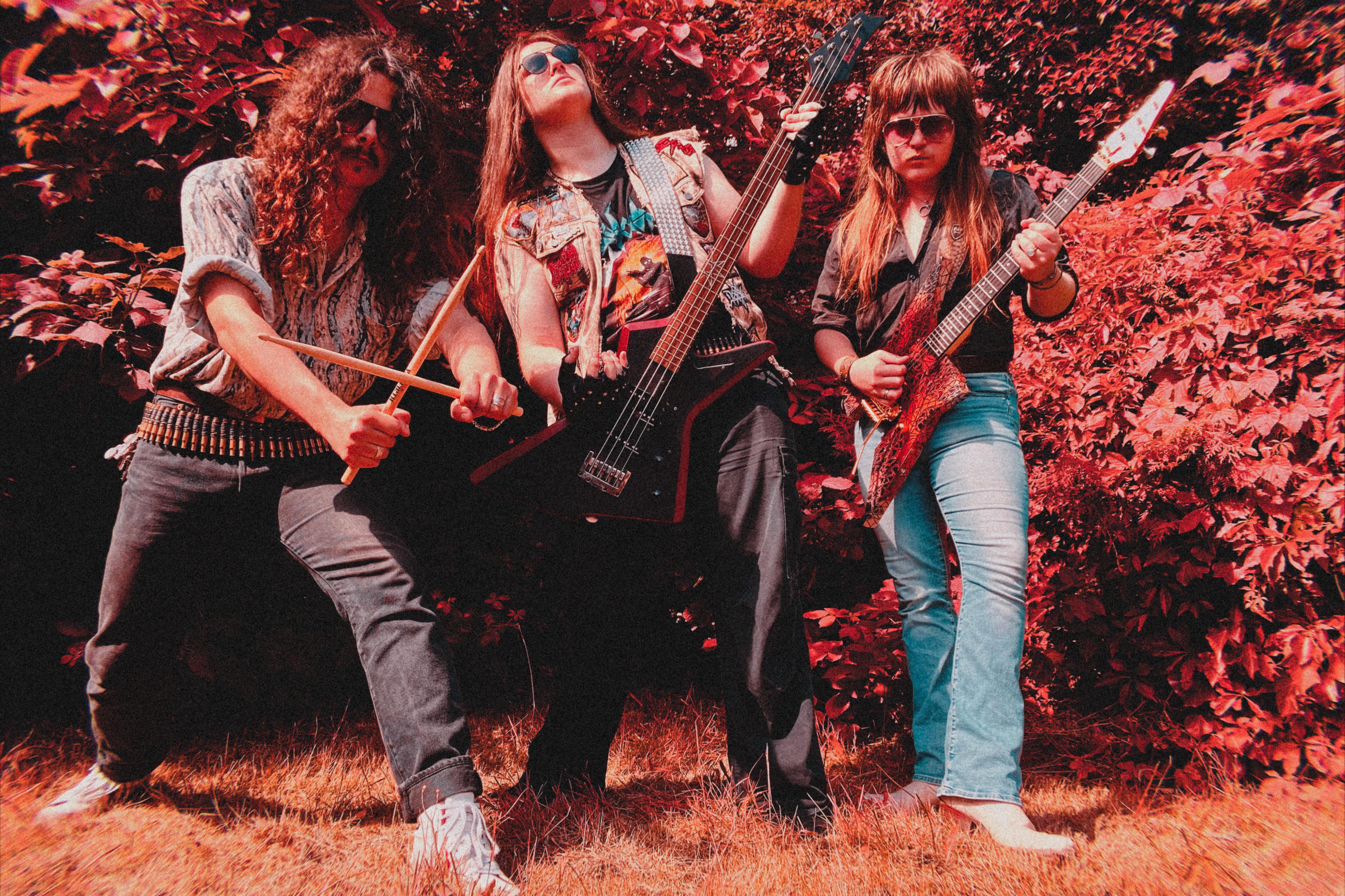 Bandfoto von der Band Manta.
Drei Typen mit langen Haaren und Sonnenbrillen und Jeans.
Die beiden links und rechts tragen Hemden. Der in der Mitte ein Bandshirt, darüber seine Kutte.
Der linke hält seine Drumsticks über Kreuz. In der Mitte wird mit seinem Bass gepost und rechts mit der Gitarre.
Im Hintergrund Gebüsch.
Das ganze Foto hat einen starken Rotstich.