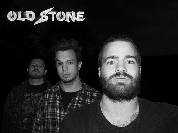 Bandphoto of Old Stone. Three guys stand diagonally behind each other in the dark and look into the camera. You can see them chest up. The image is black and white.
In the upper left corner you can see their band logo. The lettering "Old Stone" calligraphed in capital letters.