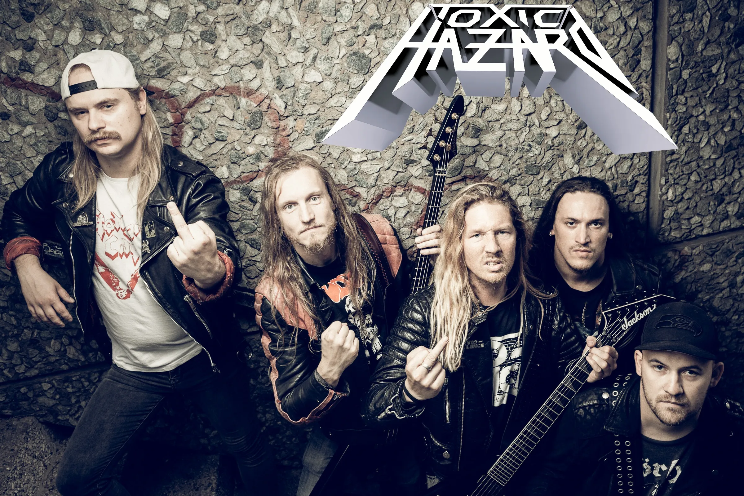 Fünf Männer stehen vor einer Steinwand und schauen rauf in die Kamera.
Einer hält einen Bass, einer eine Gitarre. Zwei zeigten Mittelfinger, einer eine Faust. Oben im Bild das Toxic Hazard Logo.