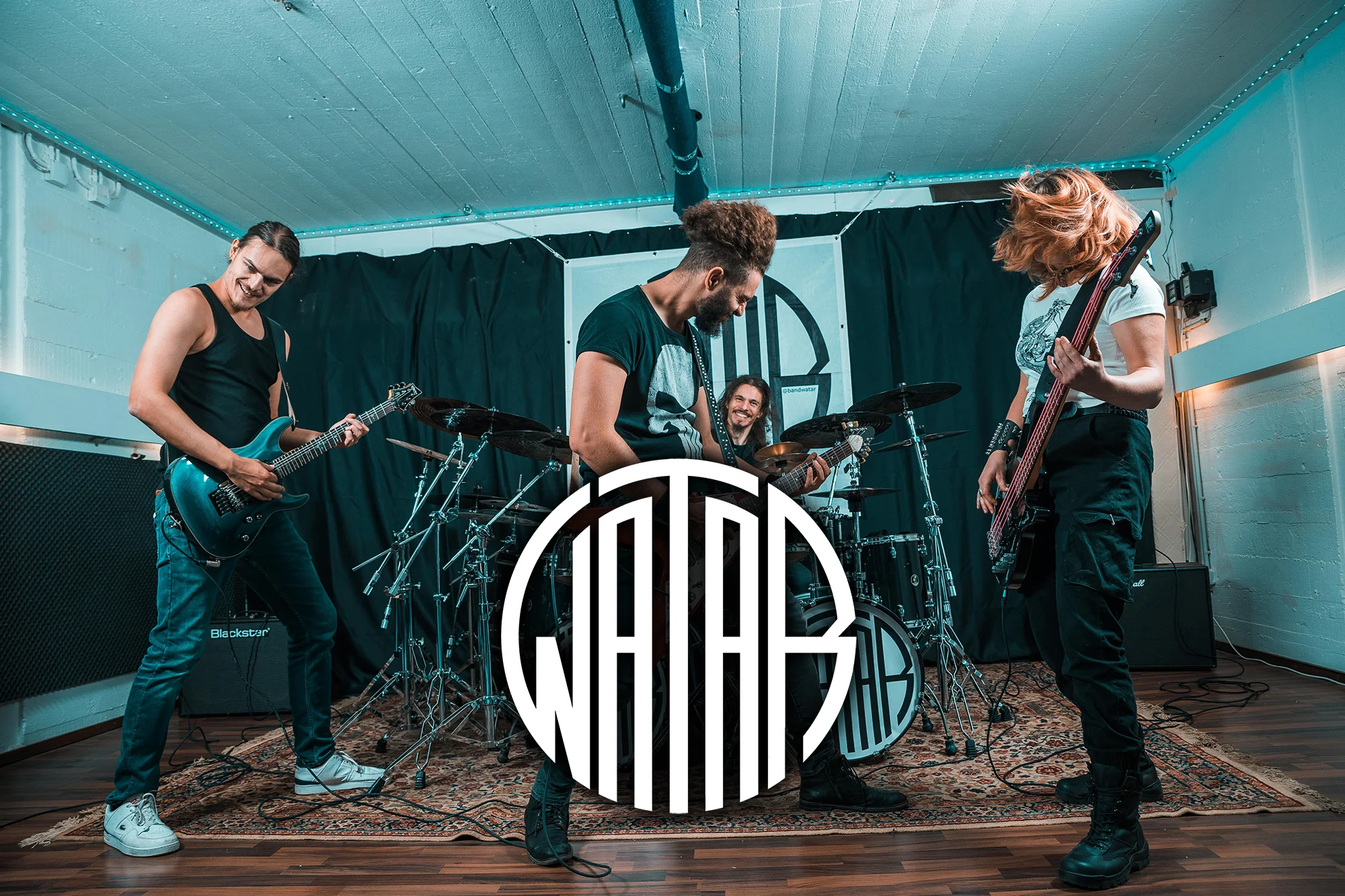 Bandphoto of Watar in their rehearsal room in action.
Two men playing guitar, one man at the drums and one woman playing bass.
In the middle in the bottom half is the Watar logo.