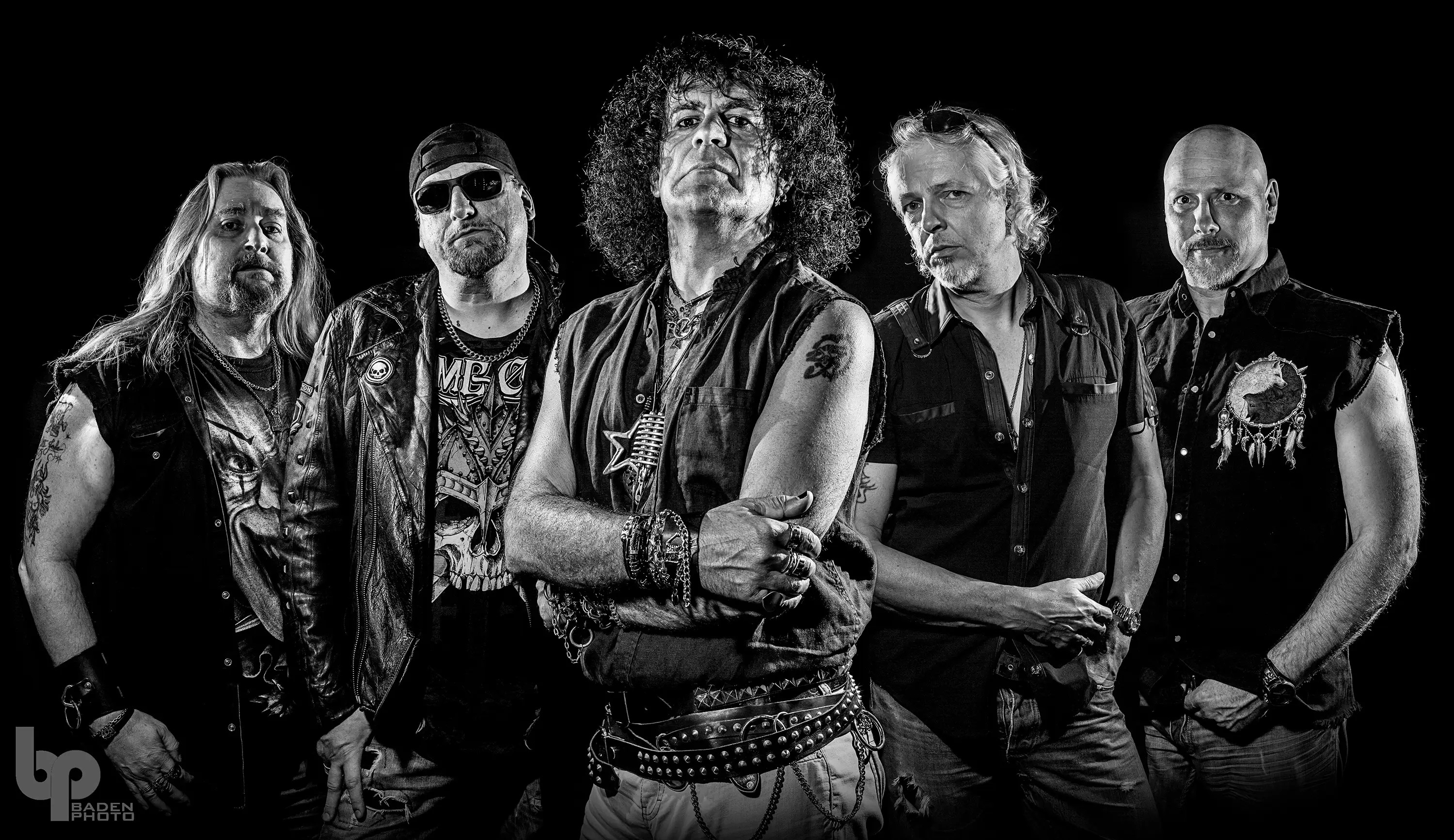 Schwarz/weißes Bandfotos von Witch Cross.
Fünf Männer stehen in V-Formation vor der Kamera.
Man sieht sie bis unter die Hüfte. Gekleidet in Kutten, Lederjacken und Nieten.