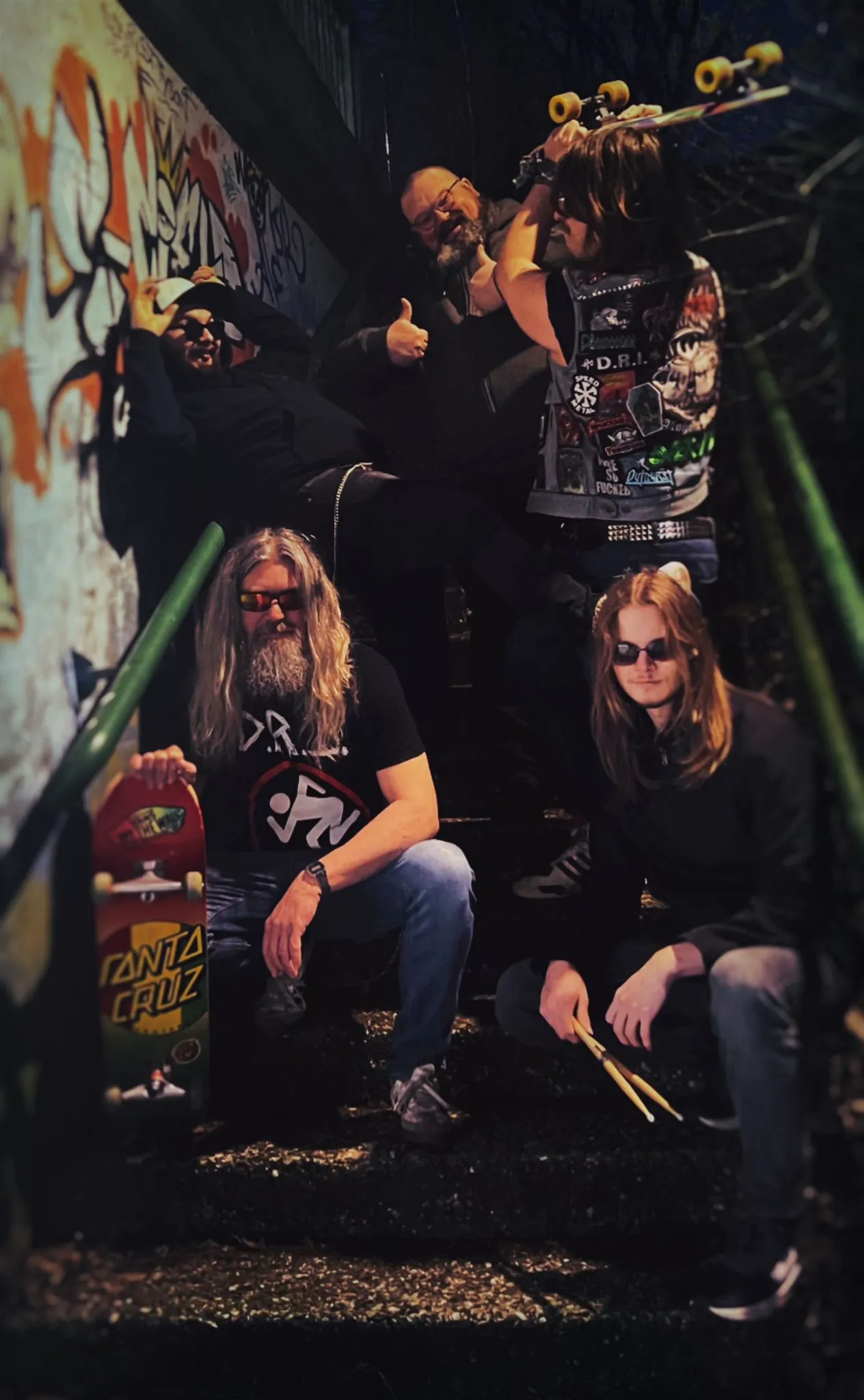 Five men on a staircase. Two are sitting, one is holding a skateboard, one is holding drumsticks.

Three are standing, one is joking, one is trying to hit another with a skateboard, and the last one is giving a thumbs-up.